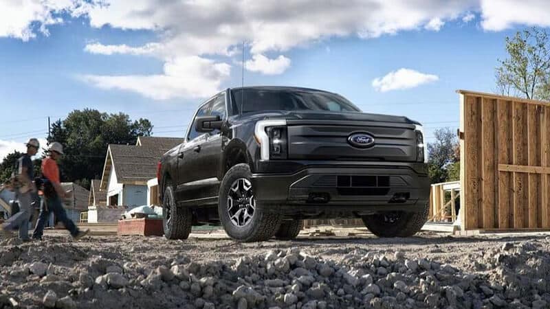 Black Ford pickup truck at a construction site with workers in the background under a blue sky.