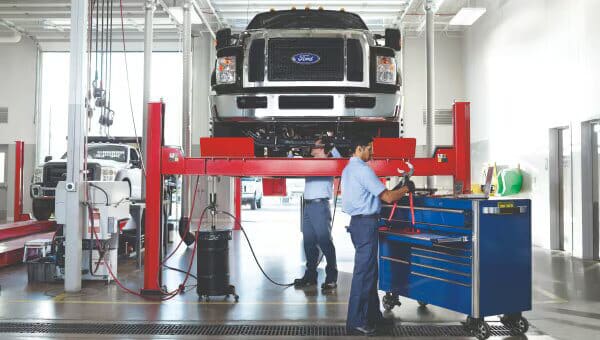 Mechanics working on a lifted truck in an auto repair shop, using tools and equipment.