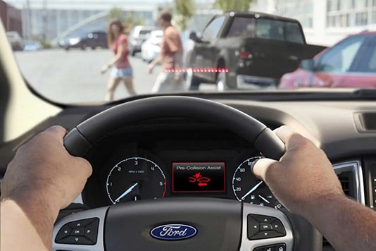 "Pre-Collision Assist alert on Ford car dashboard as pedestrians cross the street ahead."