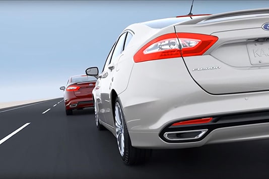 Two cars, one white and one red, driving on a highway, showcasing the rear design.