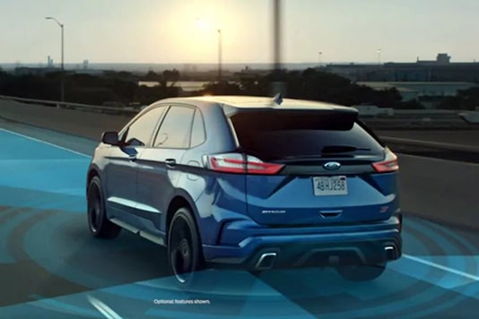 Blue SUV driving on highway with sunset, showcasing advanced driving assistance systems.