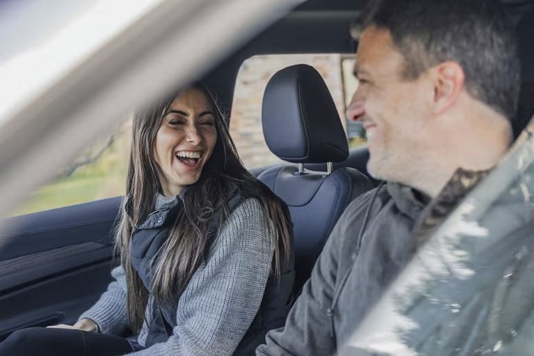 Two people smiling and laughing inside a car, enjoying a drive together.