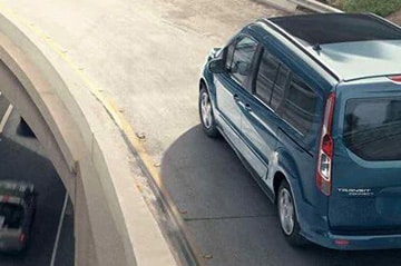Blue minivan driving on a curved highway ramp, viewed from above.