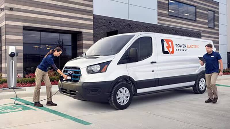 **Van with Power Electric Company logo charging outside a modern building.**