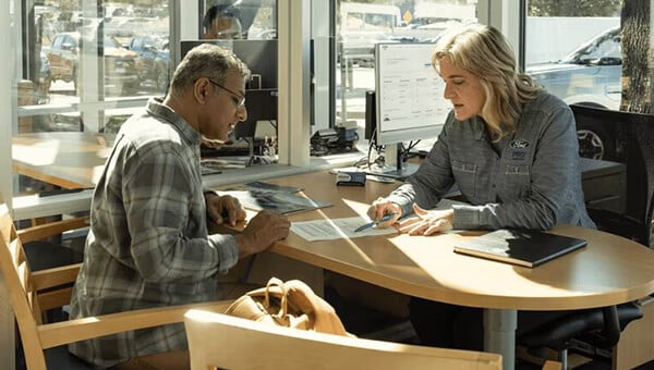 Customer interacting with a dealership employee at a desk, reviewing documents.