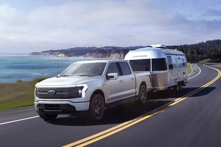 White pickup truck towing a silver Airstream trailer on a coastal highway with ocean view.