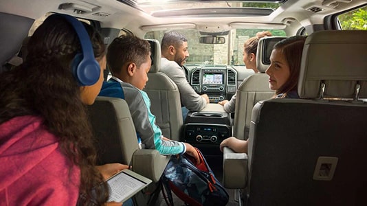 Famille discutant dans un SUV moderne, avec enfants utilisant tablette et casque audio, voyage serein.