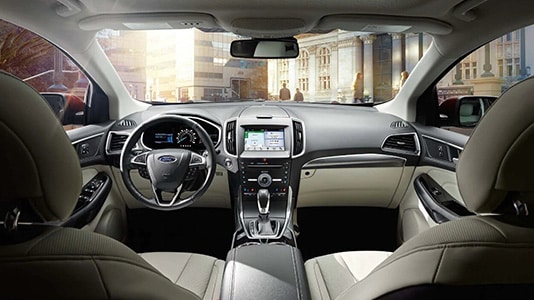 Intérieur d'une voiture moderne avec tableau de bord, volant et sièges en cuir beige, vue de la console centrale.