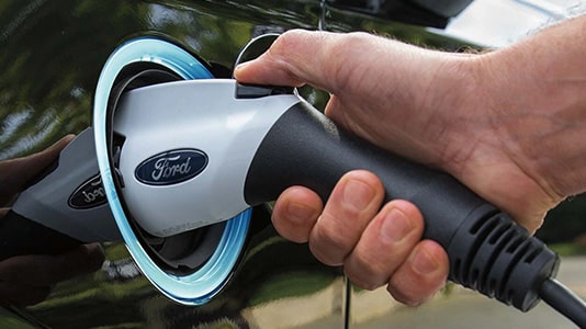 Hand plugging a Ford electric vehicle charger into a car, highlighting eco-friendly technology.