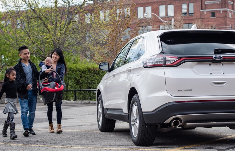 Family with children walking towards a white SUV in an urban parking lot.