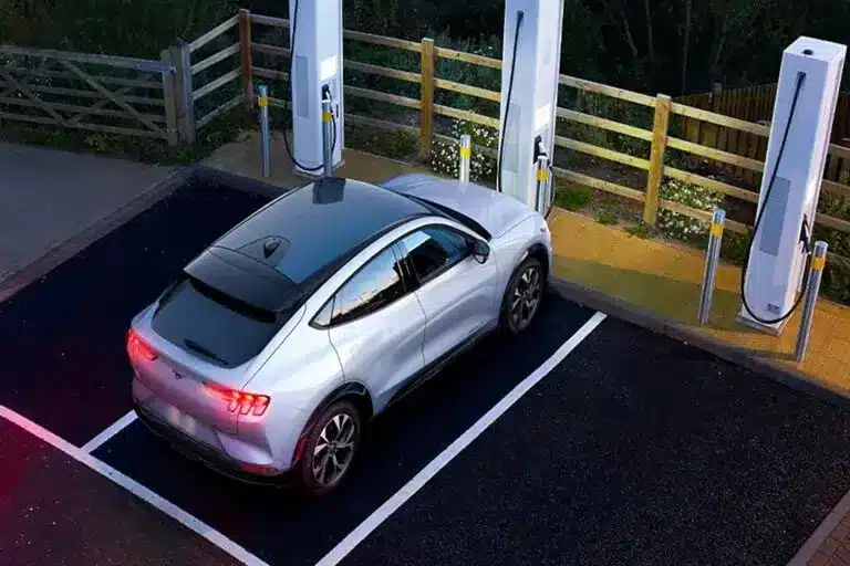 Voiture électrique argentée en train de charger à une station, entourée de trois bornes de recharge modernes.