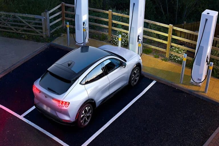 Voiture électrique grise stationnée à une borne de recharge, entourée de nature.