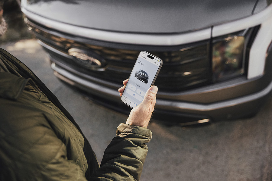 Une personne tient un smartphone affichant une application de contrôle de voiture devant un pick-up gris.