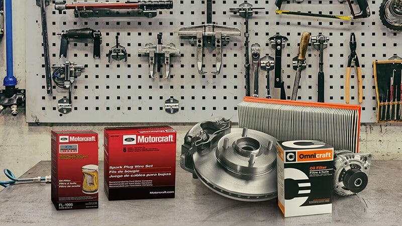 Boîte de bougies Motorcraft, filtre à huile et disques de frein sur un établi avec outils accrochés au mur.