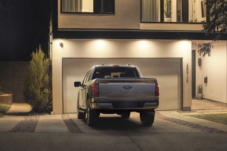 Pickup Ford F-150 gris garé devant un garage moderne éclairé la nuit. Maison contemporaine en arrière-plan.