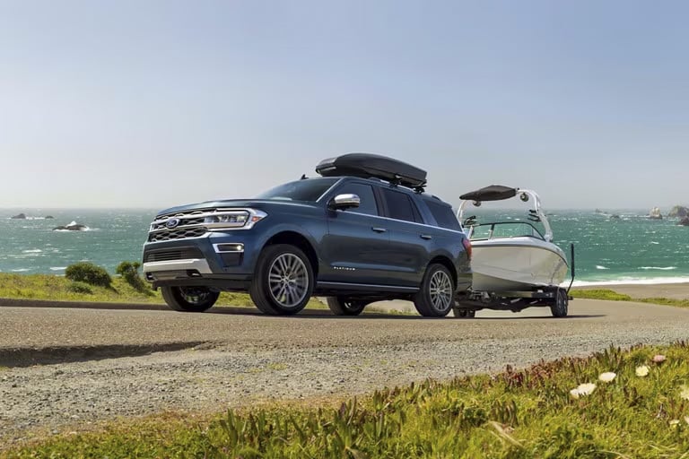 SUV bleu tractant un bateau sur une route côtière, mer en arrière-plan. Paysage marin.