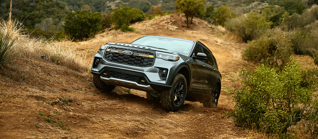 SUV gris franchissant un chemin de terre en milieu naturel. Paysage de collines et végétation en arrière-plan.