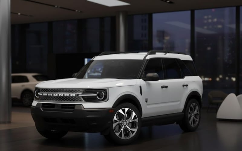 SUV blanc moderne garé dans une salle d'exposition avec des fenêtres offrant une vue urbaine en arrière-plan.